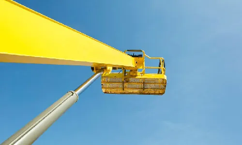 Boom lifts raised against a clear sky, work platforms extended on hydraulic booms