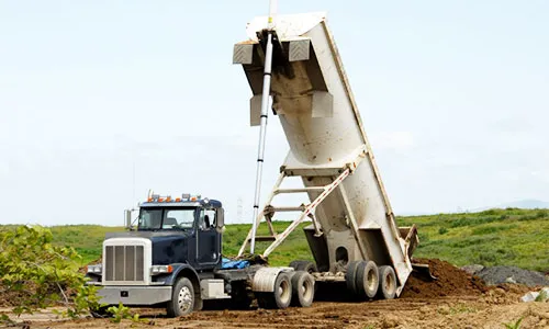 A tandem-axle dump truck with its bed hoisted, discharging a load at a jobsite