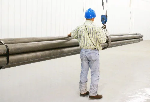 A WestCraft technician in a hard hat moving raw tube stock under an overhead hoist on the shop floor